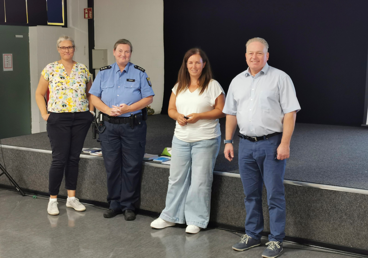 Die Referentinnen Julia Koch von der Polizeistation Langenselbold und Katja Uffelmann-Kreis von der Polizeidirektion Main-Kinzig stehen gemeinsam mit Stufenleiterin Iris Geiborg und Schulleiter Harald Klose vor der Bühne der Aula.